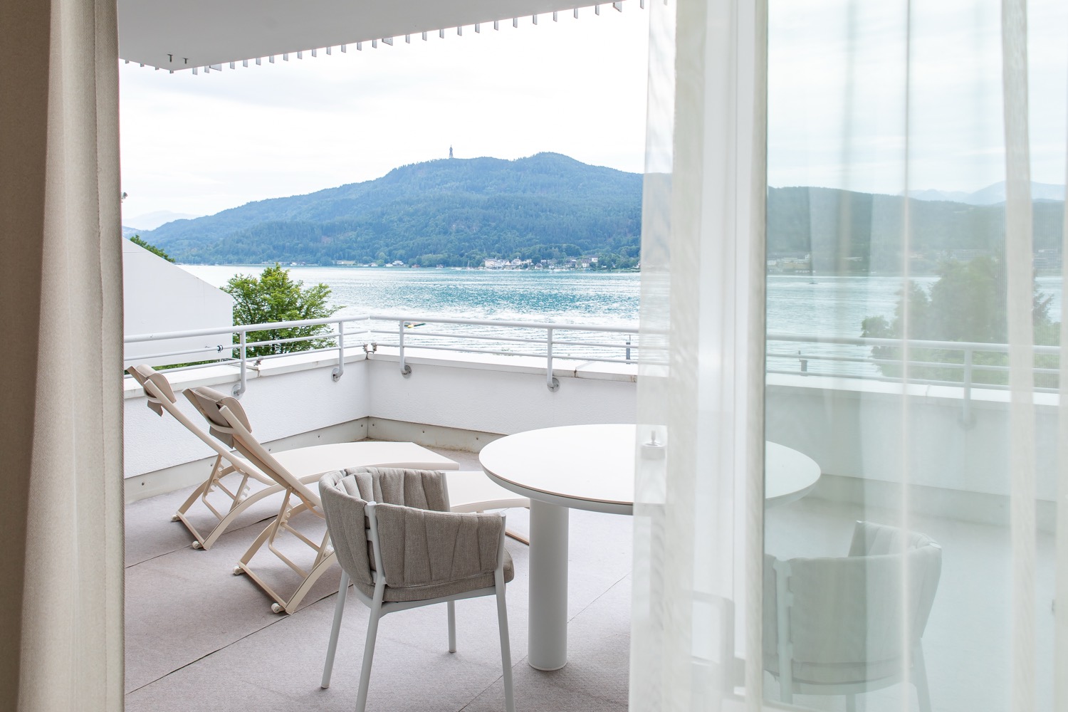 Terrasse mit Liegestühlen und Seeblick hinter leichten Vorhängen
